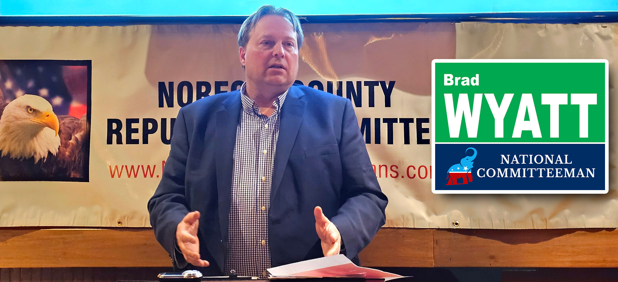 Brad Wyatt speaking at an event with eagle banner